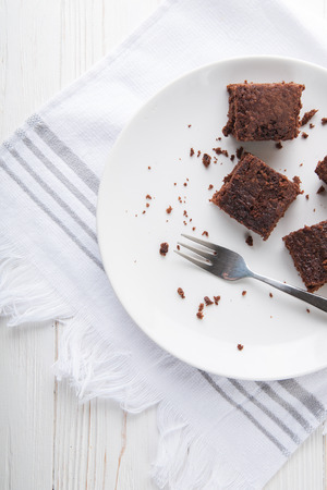 Brownie slice on a white plate on white napkin on white wooden background. Copy space. Flat lay. Overheadの写真素材
