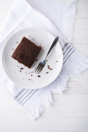 Brownie slice on a white plate on white napkin on white wooden background. Copy space. Flat lay. Overheadの写真素材