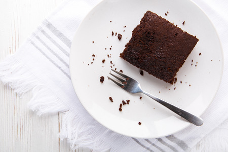 Brownie slice on a white plate on white napkin on white wooden background. Copy space. Flat lay. Overheadの写真素材