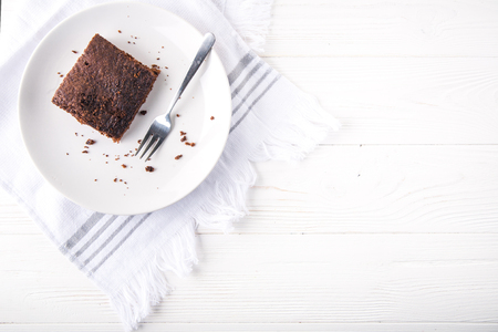 Brownie slice on a white plate on white napkin on white wooden background. Copy space. Flat lay. Overheadの写真素材