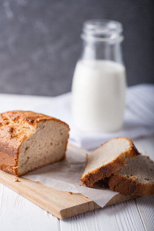 Banana bread in a pan with white parchment paper on a white wooden table with milk bottle in the background. Close up. Bakery conceptの写真素材