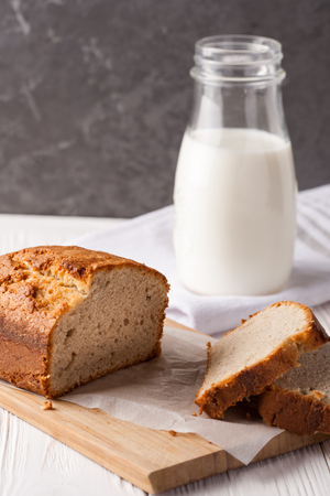 Banana bread in a pan with white parchment paper on a white wooden table with milk bottle in the background. Close up. Bakery conceptの写真素材