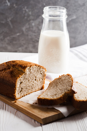 Banana bread in a pan with white parchment paper on a white wooden table with milk bottle in the background. Close up. Bakery conceptの写真素材