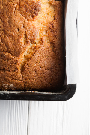 Banana bread in a pan with white parchment paper on a white wooden table. Close up. Bread cracks pattern. Bakery conceptの写真素材