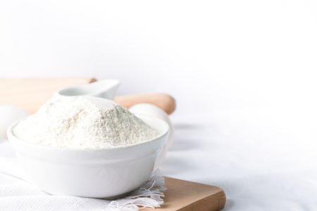 Baking ingredients. White background. Ingredients and tools to make a cake. Flour, milk, eggs, rolling pin, wooden spoons, jar. Copy space. Bakery. Baking conceptの写真素材
