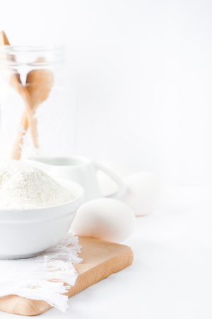 Baking ingredients. White background. Ingredients and tools to make a cake. Flour, milk, eggs, rolling pin, wooden spoons, jar. Copy space. Bakery. Baking conceptの写真素材
