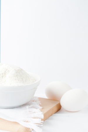 Baking ingredients. White background. Ingredients and tools to make a cake. Flour, milk, eggs, rolling pin, wooden spoons, jar. Copy space. Bakery. Baking conceptの写真素材