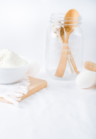 Baking ingredients. White background. Ingredients and tools to make a cake. Flour, milk, eggs, rolling pin, wooden spoons, jar. Copy space. Bakery. Baking conceptの写真素材