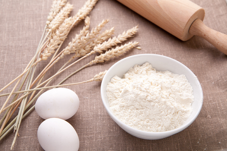 Baking ingredients. Flour, eggs, wheat and rolling pin on  table cloth. Rustic.の写真素材