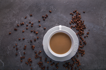 White cup of coffee with milk or tea with milk on dark grey beton background decorated with coffee beans. Copy spaceの写真素材