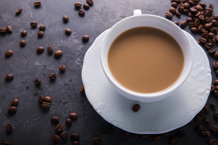 White cup of coffee with milk or tea with milk on dark grey beton background decorated with coffee beans. Copy spaceの写真素材