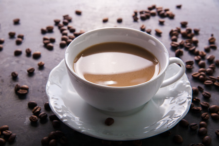 White cup of coffee with milk or tea with milk on dark grey beton background decorated with coffee beans. Copy spaceの写真素材