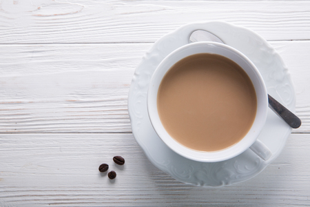 White cup of coffee with milk or tea with milk on white wooden background decorated with coffee beans. Copy spaceの写真素材