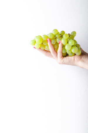 Hand holding green grapes on white background minimalism. Copy spaceの写真素材