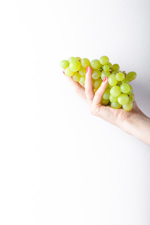 Hand holding green grapes on white background minimalism. Copy spaceの写真素材