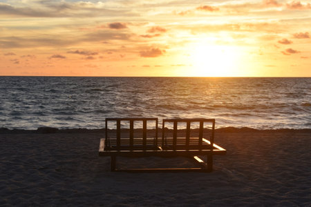 Sunset on the beach with a bench in the foreground and sea in the backgroundの写真素材