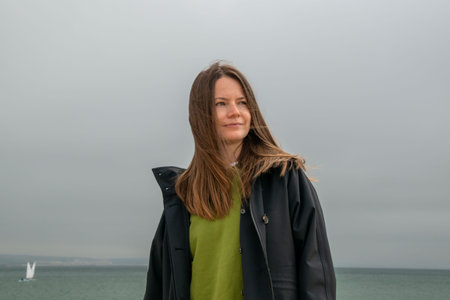 Portrait of a beautiful young woman with long brown hair in a raincoat and a green T-shirt on the...