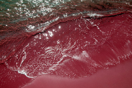 Red sand on the beach with waves of the sea in the background