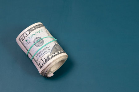 A roll of fifty dollar banknotes on a turquoise backgroundの写真素材
