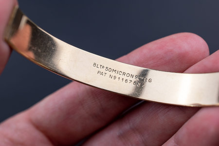 Hand holding a gold bracelet on a dark background close-up.