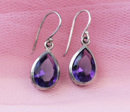 Silver earrings with purple amethyst crystals on a pink background.の写真素材