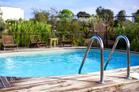 Swimming pool with blue water and wooden deck chair in the backgroundの写真素材