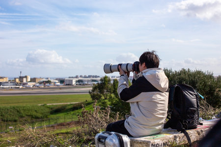 Young man sitting on a bench looking through binoculars at the airportのeditorial素材