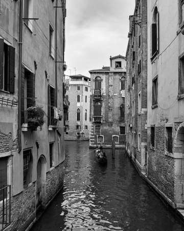 Venice, August 3, 2018. Black and white photograph of one of the city's streets and canals. Gondolier carrying tourists in his gondolaのeditorial素材