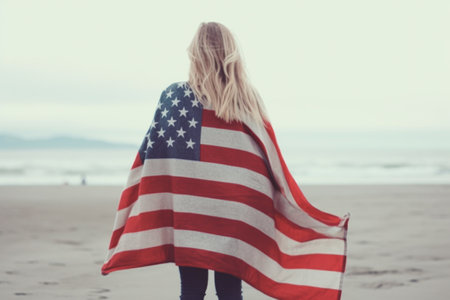 Young woman wrapped in American flag on the beach. Image with shallow depth of fieldの素材