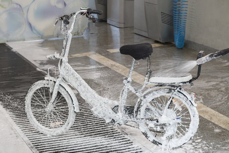 Washing an electric bicycle with a jet of foam in a car washの写真素材