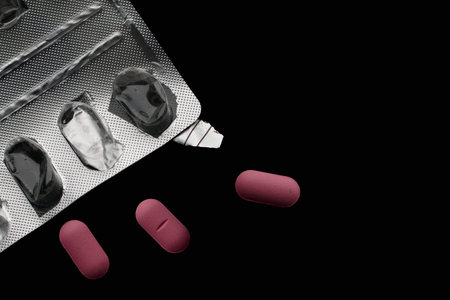 Empty blister pack and three pink pills on black background with copy space