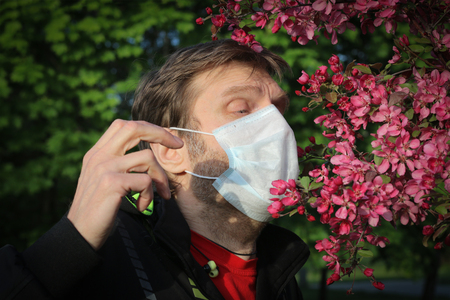 A man in a medical mask sneezes from pollen. Seasonal allergic reaction to pollenの写真素材