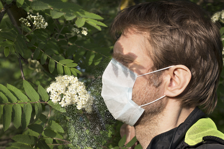 Attractive man with medical mask on his face, shadow in his eyes against pollen cloud from a flowering treeの写真素材