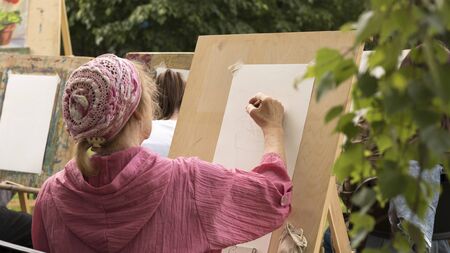 Mature woman draws floral sketch with pencil outdoors in art studio. Moscow - June 1, 2019. Hobby for retired people, social programs for elderly people. Selective focus. 16:9 imageのeditorial素材