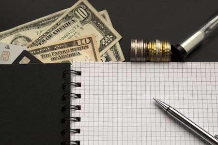 Blank page with pen, dollars, coins, credit cards, sand glass on the black background. Planning, budgeting conceptの写真素材