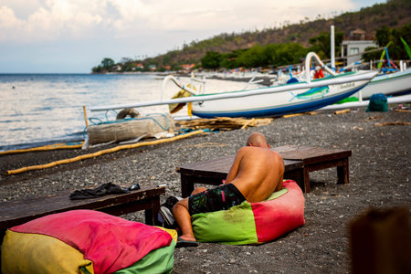 BALI, INDONESIA - December 01, 2019: Tourist relaxing in typical small Black Sand Beach cafe on Bali