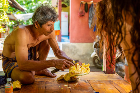 BALI, INDONESIA - November 30, 2019: Local balinese man cut exotic fruit durian in his house to...