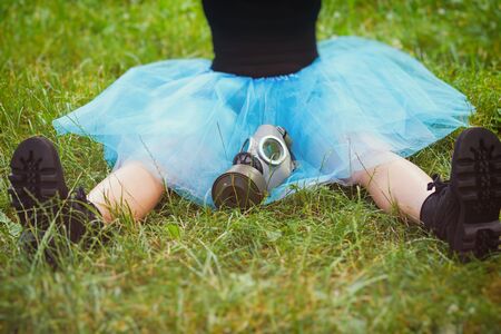 Woman in blue skirt with gas mask sits on green grass. Environmental protection, biohazard and ecological conceptの写真素材