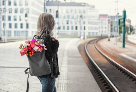 Young woman with backpack with bouquet of flowers waiting a train. Photo from the back.の写真素材