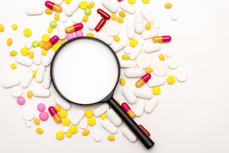 The magnifier and pills on white background. Health, medicine and science concept. Top viewの写真素材