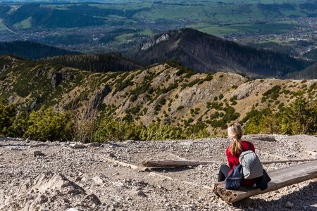 Woman is sitting on a wooden bench and enjoying a great view of mountain landscape. Mountain Hiking. Tatra mountains, Poland. Local travel conceptの写真素材