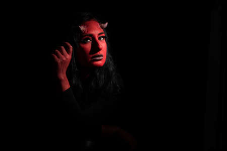 Halloween concept. Demon woman with red face and small horns on black background with copy space. Ideas for halloween body artの写真素材