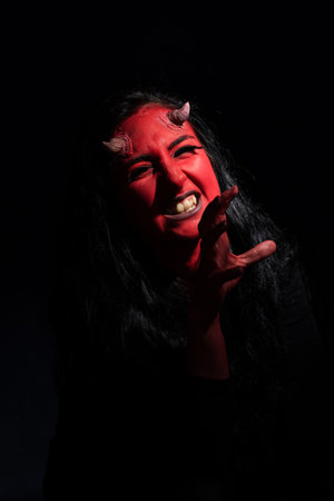 Halloween concept. Demon woman with red face and small horns on black background with copy space....