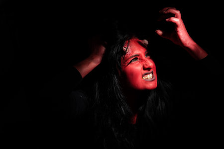 Halloween concept. Demon woman with red face and small horns on black background with copy space....