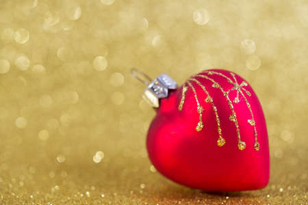 christmas bauble in a shape of heart on yellow blurred glitter background with copy spaceの写真素材