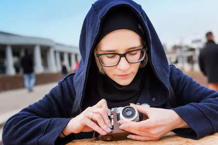 portrait of young pretty woman with retro camera in leather case outside in a autumnal city park. Outdoor lifestyle portrait of young hipster woman taking photo.の写真素材