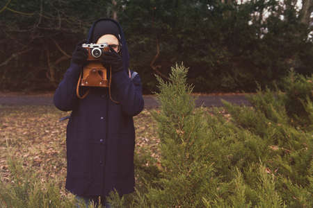 portrait of young pretty woman with retro camera in leather case outside in a autumnal city park. Outdoor lifestyle portrait of young hipster woman taking photo.の写真素材