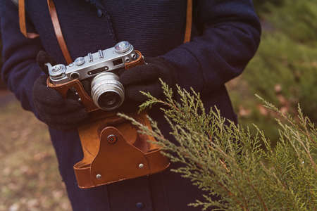 Close up of young woman hipster holding retro film camera in hands. Woman's hands holding an old retro camera at nature background.の写真素材