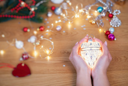 Christmas concept. Human hands hold a ceramic christmas decoration in a shape of glowing heart with...