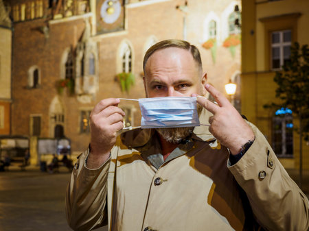 Adult man wearing mask walking in a night european city. Mask is a necessary thing in new normal...